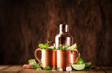 Limon, buz, zencefil birası, votka ve naneli bakır bardakta Moskova katırı kokteyli. Ahşap arkaplan, çubuk araçları, negatif boşluk