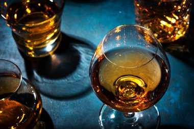 Sert alkollü içecekler, sert içkiler, bardakta içki ve damıtma iseti: konyak, viski ve diğer şeyler. Mavi arkaplan, üst görünüm 