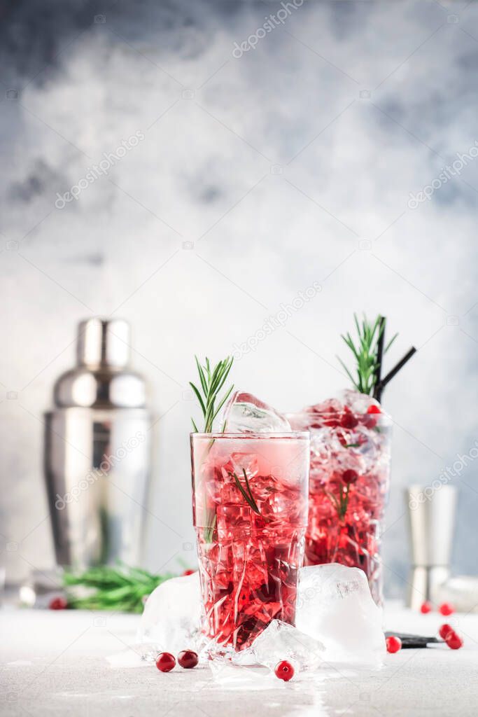 Cranberry cocktail with vodka, ice, juice, rosemary and red berries in highball glass. Refreshing long drink. Gray table background with negative space
