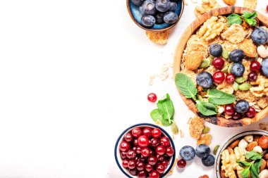 Sağlıklı kahvaltı için şekersiz müsli ve malzemeler. Granola, fındık, yabanmersini, yaban mersini, Yunan yoğurdu, beyaz masada tam tahıl gevreği, üst manzara.
