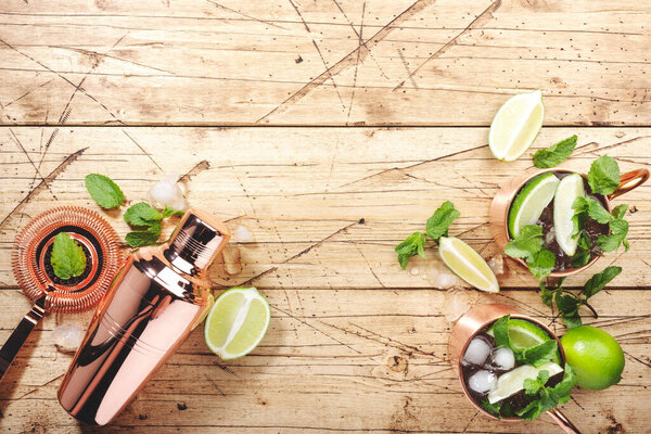 Коктейли московских мулов в медной кружке с лаймом, льдом, имбирным пивом, водкой и мятой. Водяной фон, барные инструменты, отрицательное пространство, вид сверху