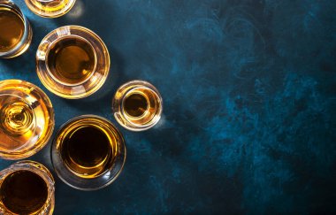 Sert alkollü içecekler, sert içkiler, bardakta içki ve damıtma iseti: konyak, viski ve diğer şeyler. Mavi arkaplan, üst görünüm 