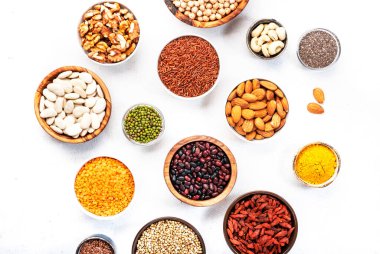 Süper yiyecekler, baklagiller, tahıllar, fındıklar, beyaz masadaki kaselerdeki tohumlar. Boşluğu kopyala, üst görünüm