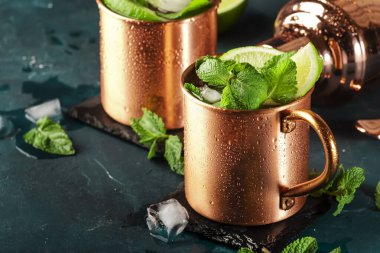 Limon, buz, zencefil birası, votka ve naneli bakır bardakta Moskova katırı kokteyli. Koyu mavi arkaplan ve çubuk araçları