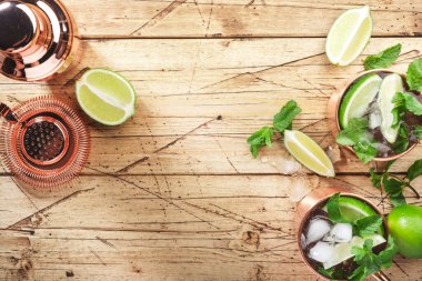 Limon, buz, zencefil birası, votka ve naneli bakır bardakta Moskova katırı kokteyli. Ahşap arkaplan, çubuk araçları, negatif boşluk, üst görünüm