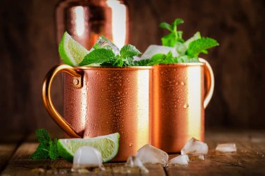 Limon, buz, zencefil birası, votka ve naneli bakır bardakta Moskova katırı kokteyli. Ahşap arkaplan, çubuk araçları, negatif boşluk