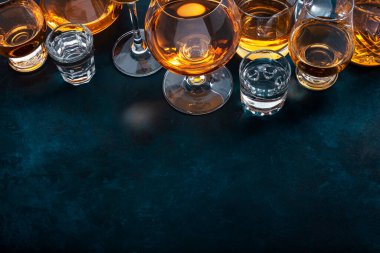 Sert alkollü içecekler, sert içkiler, bardakta içki ve damıtma iseti: konyak, viski ve diğer şeyler. Mavi arkaplan, üst görünüm 