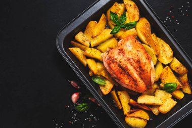 Koyu arka planda fırında tavuk göğsü ve fırın kabında altın patatesler.