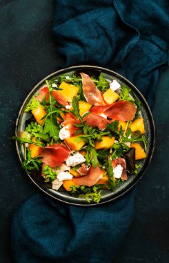 Kavunlu taze salata, prosciutto, yumuşak peynir ve roka mavi arka planda, üst manzara, kopyalama alanı