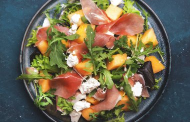 Kavunlu taze salata, prosciutto, yumuşak peynir ve roka mavi arka planda, üst manzara, kopyalama alanı