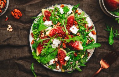 İncirli salata, keçi peyniri, ceviz, pazı ve roka kahverengi arka planda, üst manzara, kopyalama alanı