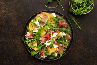 Kavunlu salata, jamon, keçi peyniri ve roka kahverengi arka planda, üst manzara, kopyalama alanı