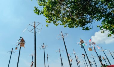 North Jakarta, Indonesia. August 17, 2025. A low-angle view. A group of Asian young men celebrates their victory in the traditional panjat pinang (greased pole climbing) competition under a clear blue sky adorned with thin white clouds.