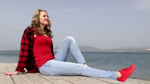 Girl and sea. Woman sit on a pier. Blue sea. Good weather. Girl resting on the sea. girl looks at the sea. Calm sea. Rest. Relax. Bask in the sun. Enjoy the sun. Wind waving hair. romantic girl. — Stock Video