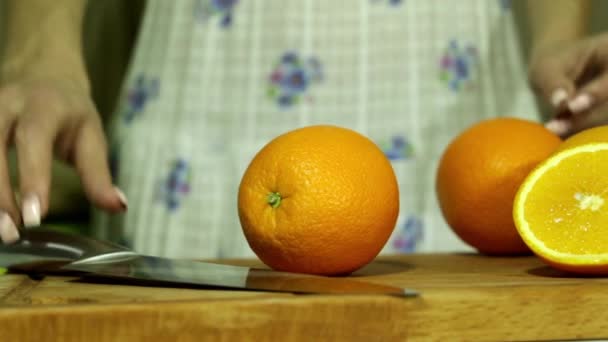 Frau schneidet Orange. Weibchen schneiden Orange in zwei Teile. Großes Messer. in der Küche. Holzbrett. Haus stolze Frau. frische Orange. frisches Obst. Scharfes Messer. wunderschöne Orangen. tropischer Geschmack. — Stockvideo