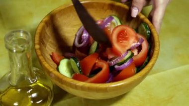 Woman mixing salad. Female hands mix vegetables. Wooden spoon. Wooden salad bowl. Fresh vegetables. Olive oil. Tomatoes, cucumbers, onion. bamboo bowl. In the kitchen. house-proud woman.