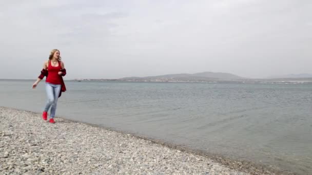 Ragazza che cammina sulla spiaggia. Ragazza e mare. Gioia, spensieratezza, svago. spiaggia rocciosa. Mare calmo. La costa. spiaggia deserta. goditi il mare. goditi la solitudine. lanciare pietre in mare. ciottoli . — Video Stock