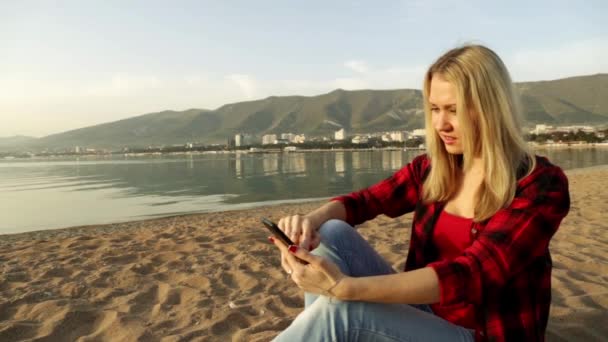 Una donna sulla spiaggia con il telefono. Internet mobile. Cellulare. social network. Smartphone. Cellulare. Buonasera mare. Mare. Spiaggia di sabbia. WhatsApp. comunicazione mobile . — Video Stock