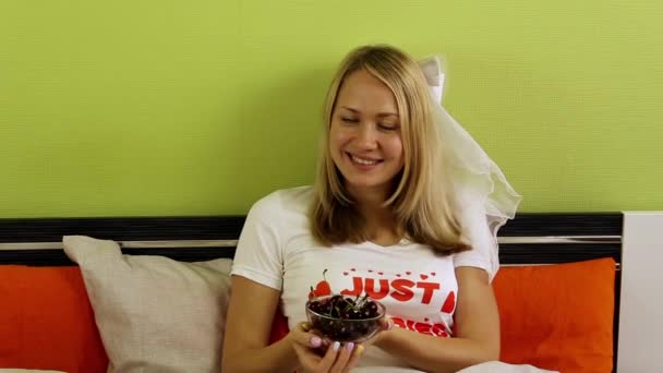 Novia comiendo cereza en la cama. Jovencita feliz acostada en la cama. Baya sabrosa, cerezas jugosas para el desayuno. Acabo de casarme, recién casados. Luna de miel — Vídeos de Stock