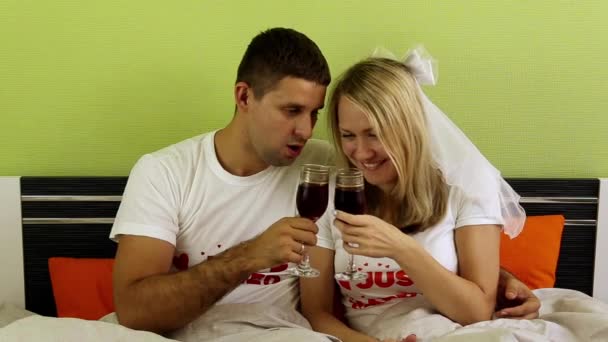 Un par bebiendo vino en la cama. Pareja joven bebiendo vino en el dormitorio. Pareja cariñosa relajándose en la cama, romance. Acabo de casarme, recién casados, recién casados. Luna de miel, familia joven . — Vídeos de Stock