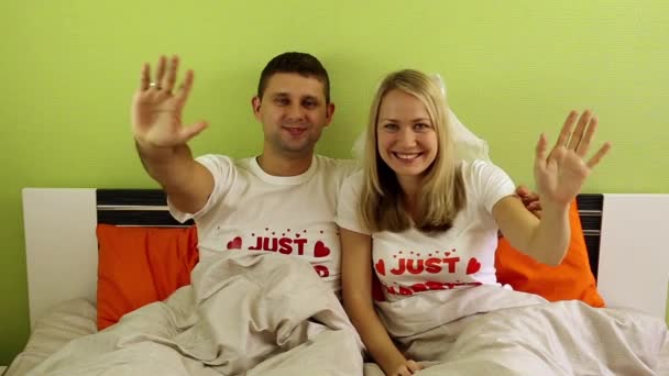 Um casal feliz. Casal jovem acenando alegremente para a câmera. Um jovem casal amoroso na cama. Casados, lua-de-mel, recém-casados. Lua-de-mel, família jovem — Vídeo de Stock