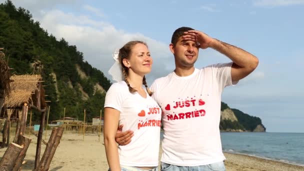 Verliefde paar in de buurt van de zee. De pasgetrouwden op het strand. Man en vrouw knuffelen op het strand. Huwelijksreis, romantiek, net getrouwd — Stockvideo