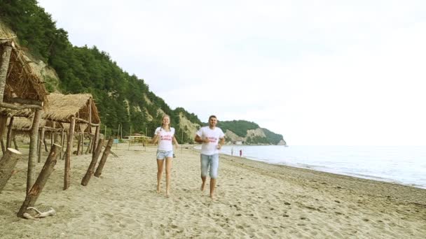 Una pareja encantadora corriendo por la playa. Recién casados corriendo por el mar. Luna de miel, romance, recién casados . — Vídeos de Stock