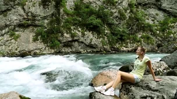 Tjejen sitter på en bakgrund av en berg flod. Kvinna och berg flod. Tjejen sitter på stranden av floden snabb ren. — Stockvideo