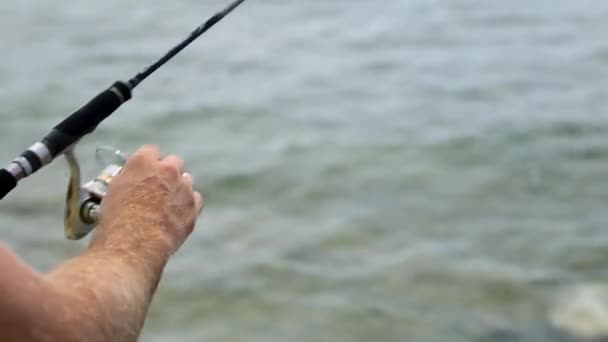 Pesca marítima. Carrete giratorio. Un hombre pescando en la costa. Pescador con spinning. La mano gira el carrete girando . — Vídeo de stock