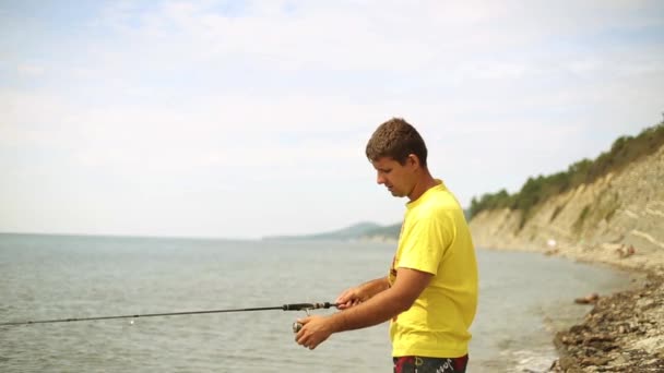 Hombre con spinning captura de peces. Pesca en el mar a Spinning. El hombre lanza giros. Pescador en la playa . — Vídeo de stock