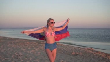 Deniz kıyısında Rusya bayrağı taşıyan bikinili genç seksi kadın.