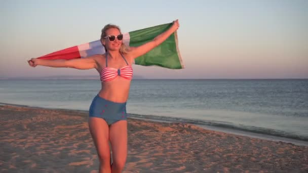 해변에 있는 이탈리아 국기를 들고 비키니를 입고 있는 젊은 여성 — 비디오