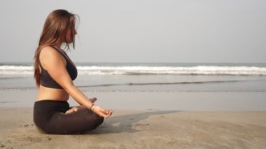 Lotus pozisyonundaki çekici kadın deniz sahilinde meditasyon yapıyor.