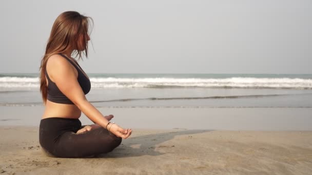 Приваблива жінка в позі лотоса медитує на морському пляжі — стокове відео