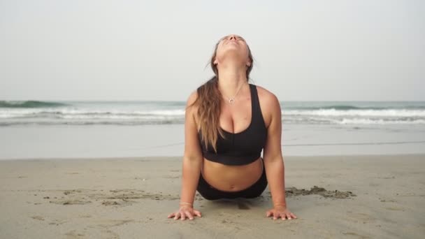 Молода приваблива жінка-інструктор йоги, тренується на тлі моря — стокове відео