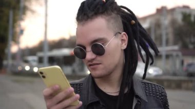 Rasta saçlı modern genç adam açık havada akıllı telefon kullanıyor.