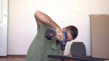 Genç bir adam elektrikli tornavidayla yeni ahşap mobilyalar monte ediyor.