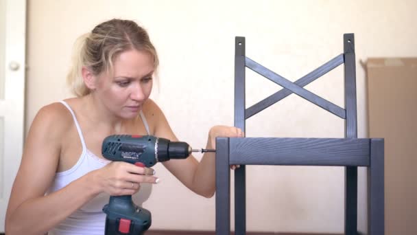 Jonge vrouw huisvrouw assembleert nieuwe houten meubels met behulp van een elektrische schroevendraaier — Stockvideo