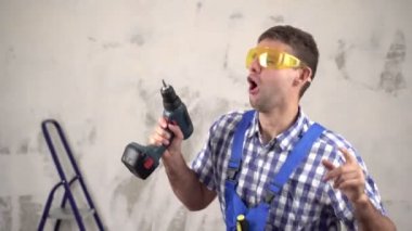 Evin arka planında dans eden neşeli inşaat işçisi. Komik inşaatçı. Tamirci elektrikli tornavidayla dans ediyor.