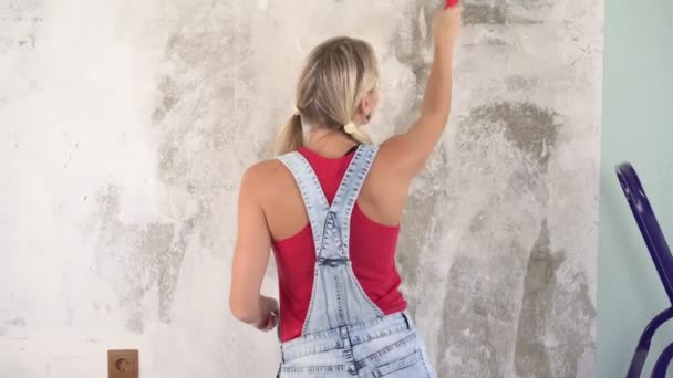 Uma jovem mulher faz reparos em casa, cola o papel de parede e mostra um polegar para cima — Vídeo de Stock