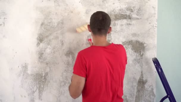 Ein Mann repariert und klebt Tapeten an die Hauswand — Stockvideo