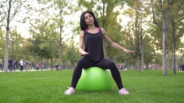 Ελκυστική σπορ γυναίκα κάθεται στο fitball και πηγαίνει για σπορ και fitness στο πάρκο — Αρχείο Βίντεο