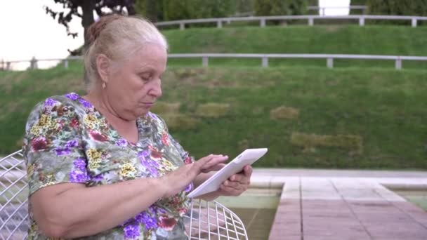 Un anziano in pensione usa un tablet all'aperto. La nonna sta imparando ad usare le moderne tecnologie digitali — Video Stock