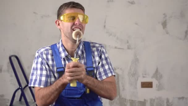 Vrolijke en gelukkige mannelijke bouwer of arbeider zingt tegen de achtergrond van reparaties in het huis, slow motion — Stockvideo