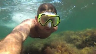 Maskeli genç bir erkek dalgıç denizin altında yüzüyor.