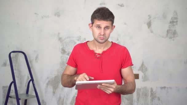 Ένας άνθρωπος με ένα tablet υπολογιστή στο παρασκήνιο των επισκευών στο σπίτι — Αρχείο Βίντεο