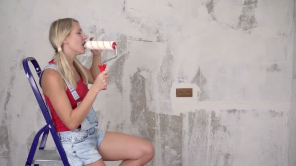 Young happy woman sits on a stepladder and sings on the background of renovations in the house — Stock Video