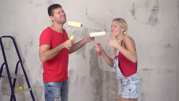 Casal feliz, homem e mulher, cantando no fundo da renovação da casa. Jovem família alegre se divertindo durante a renovação e o aquecimento doméstico — Vídeo de Stock