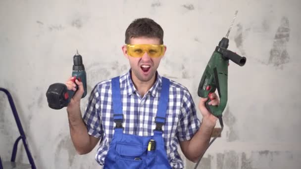 Lustige fröhliche emotionale männliche Arbeiter oder Bauarbeiter mit elektrischen Werkzeugen auf dem Hintergrund von Reparaturen im Haus — Stockvideo