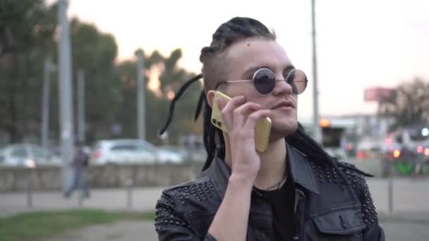 Сучасний молодий панк чоловік гуляє по місту і розмовляє по телефону — стокове відео
